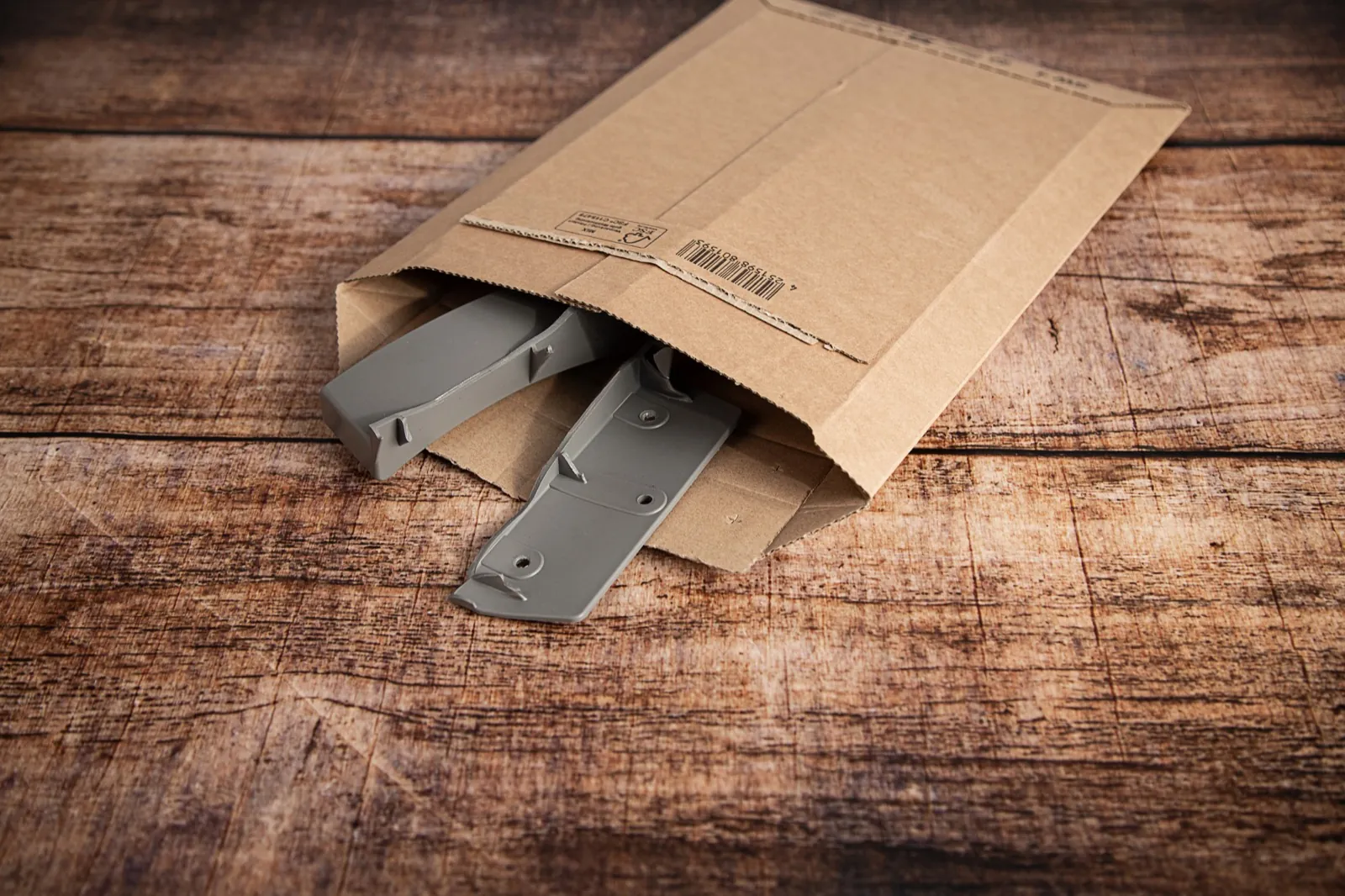 A broken grey plastic part packed in a cardboard mailer, ready to post